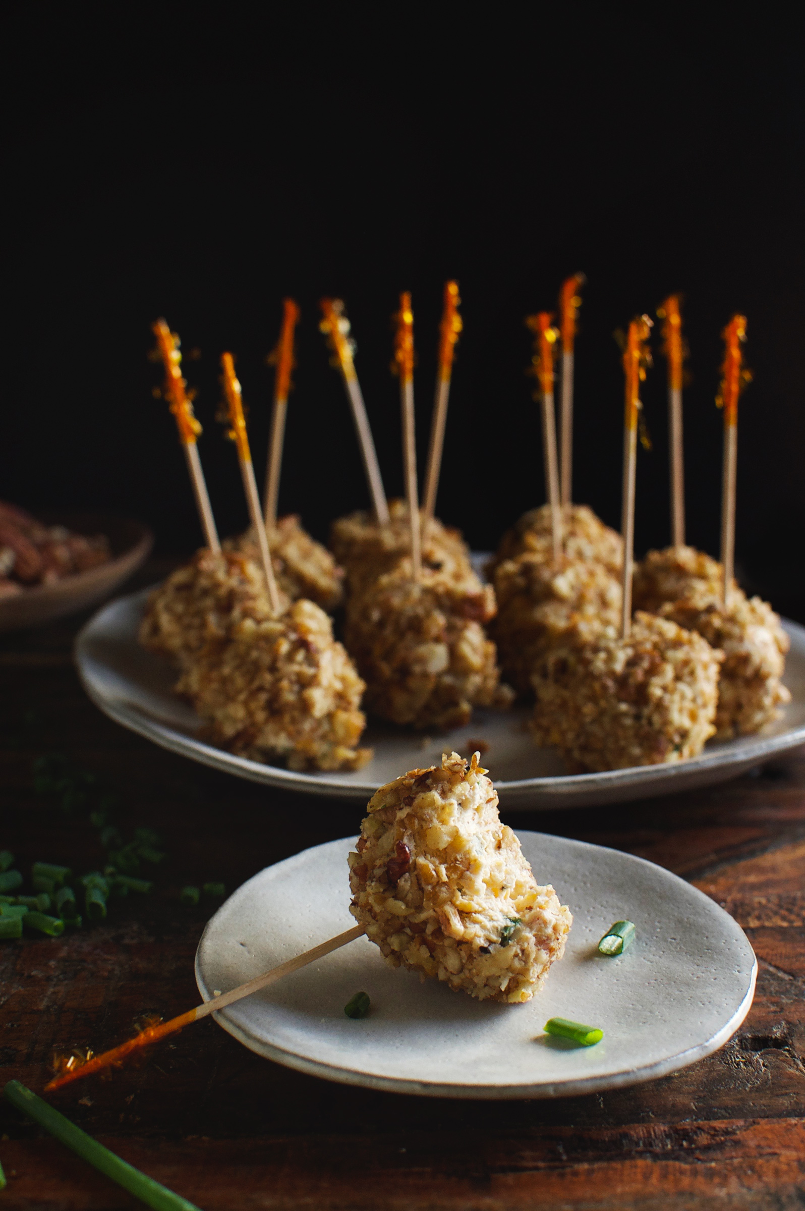 Low-Carb Mini Bacon Chive Cheeseballs on a plate with party picks. One is on a small plate with a bite taken out.