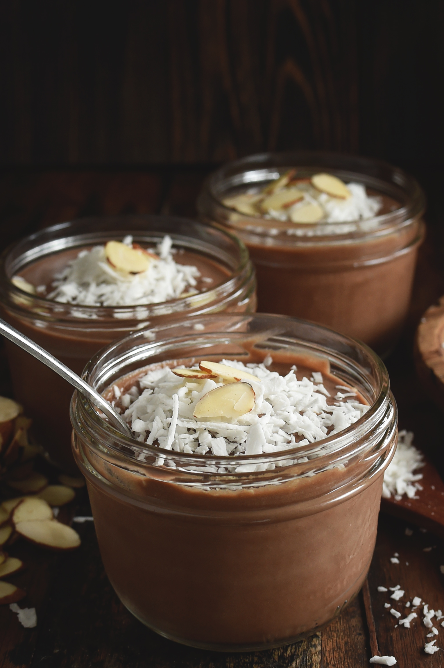 Chocolate Almond Avocado Pudding- three jars full with a spoon in one.
