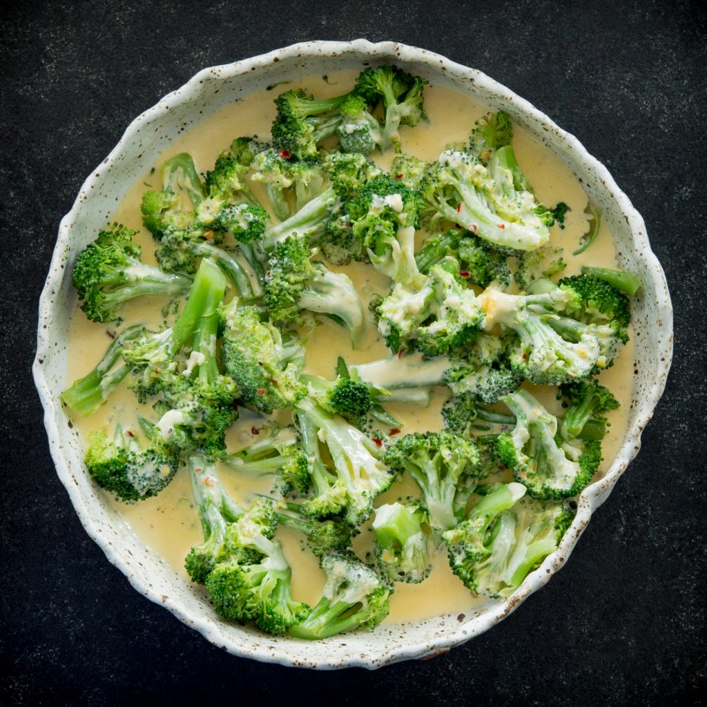 Adding cheese sauce to a plate of steamed broccoli.