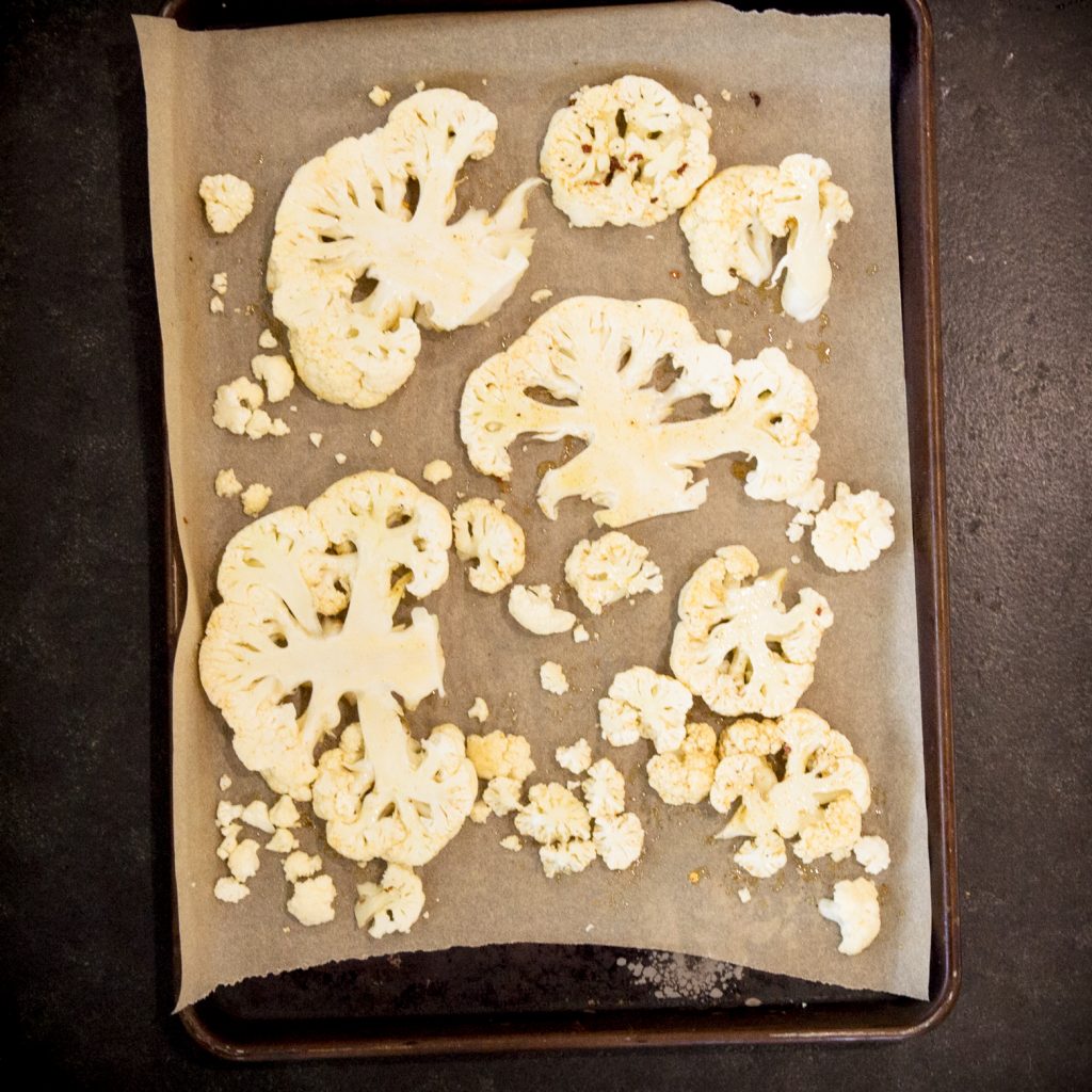 Slices of cauliflower on tray coated with oil.