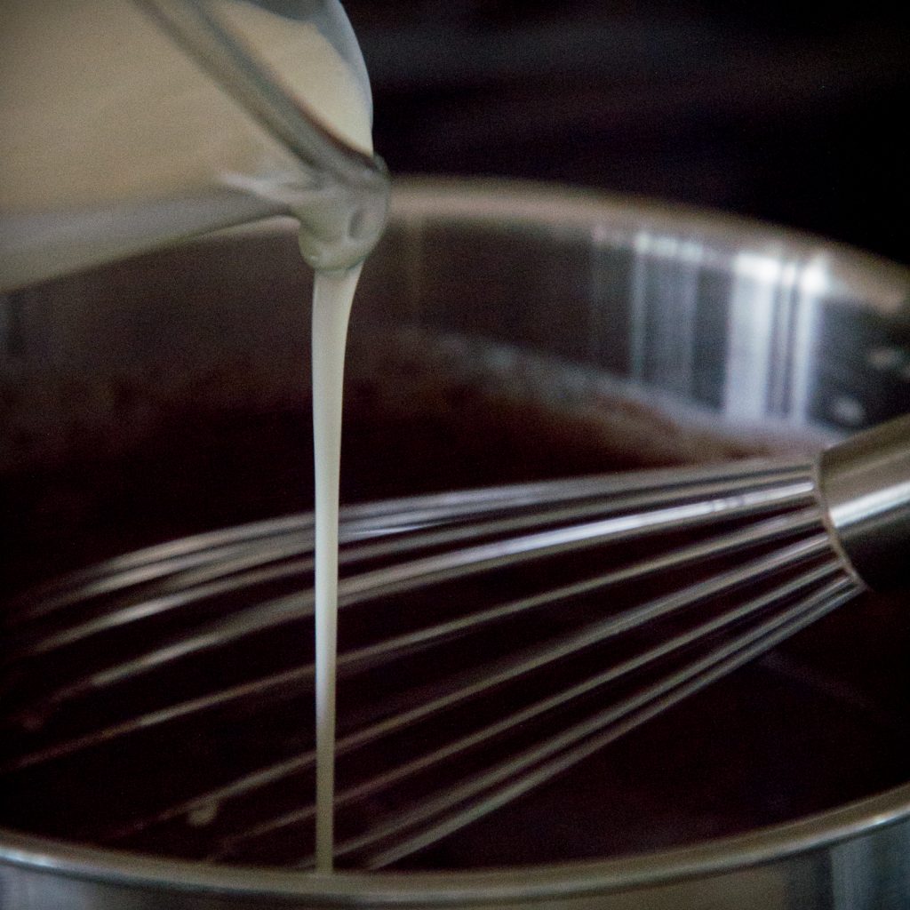 Pouring milk into saucepan with wire whisk.