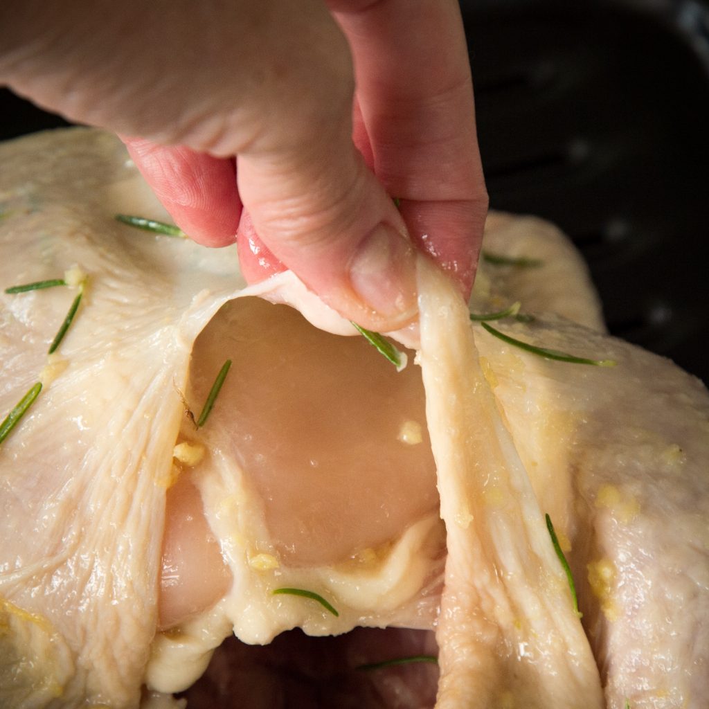 Raw chicken with the skin being pulled up.