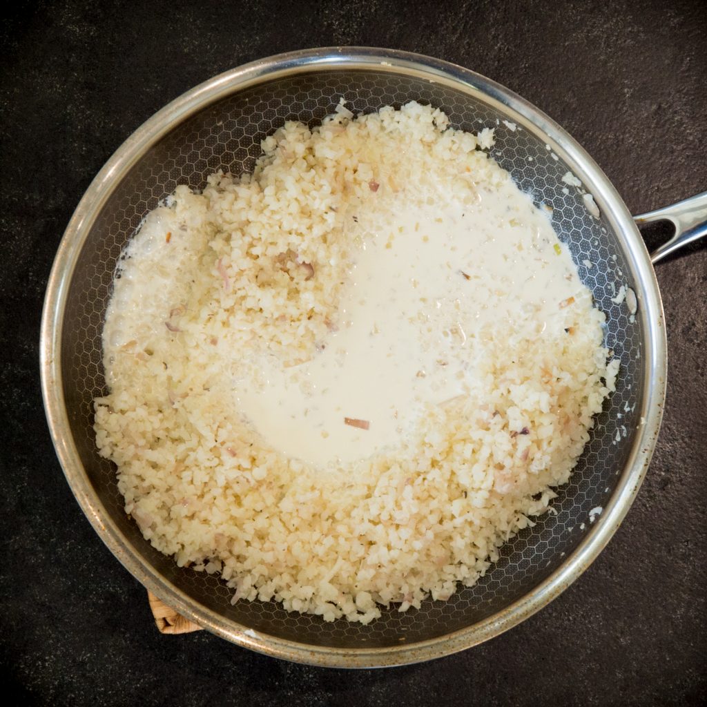 Adding cream to the cauliflower risotto in the pan.
