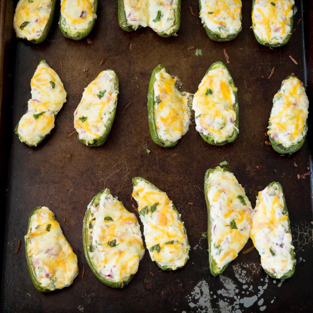 Process photo of jalapeño poppers on a baking tray with grated cheese on top.