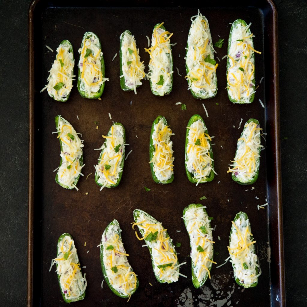 Process photo of jalapeño poppers on a baking tray with grated cheese on top.