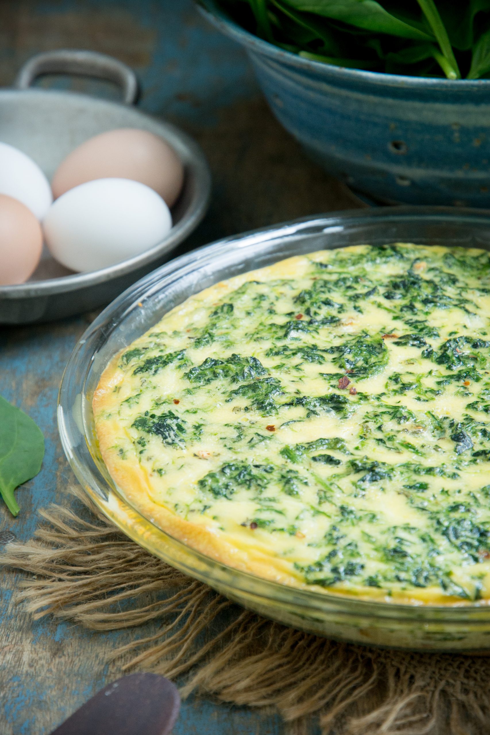 Close up photo of Crustless Spinach Quiche on a plate with eggs on the background.
