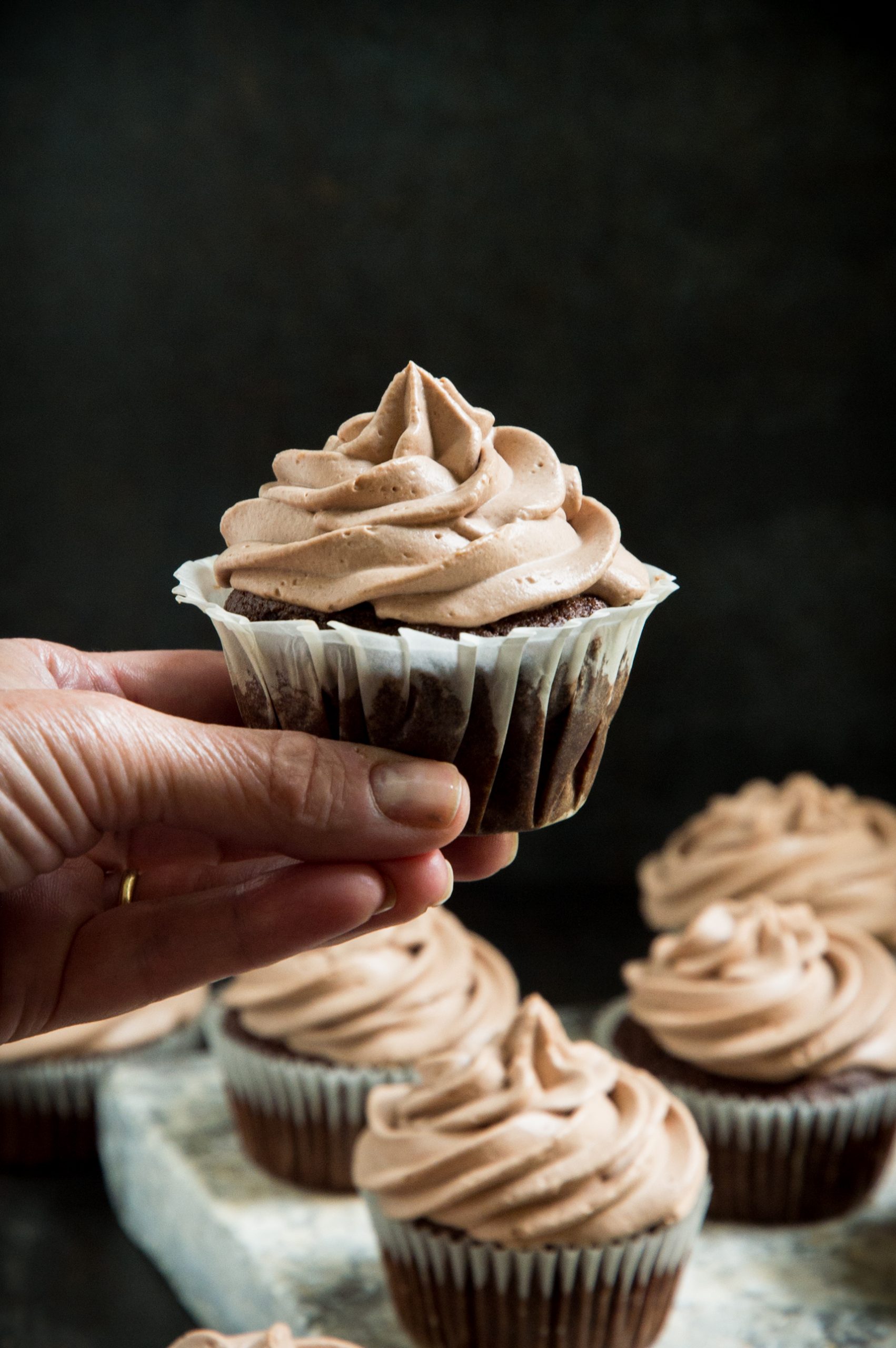 Hand holding up a frosted chocolate cupcake 