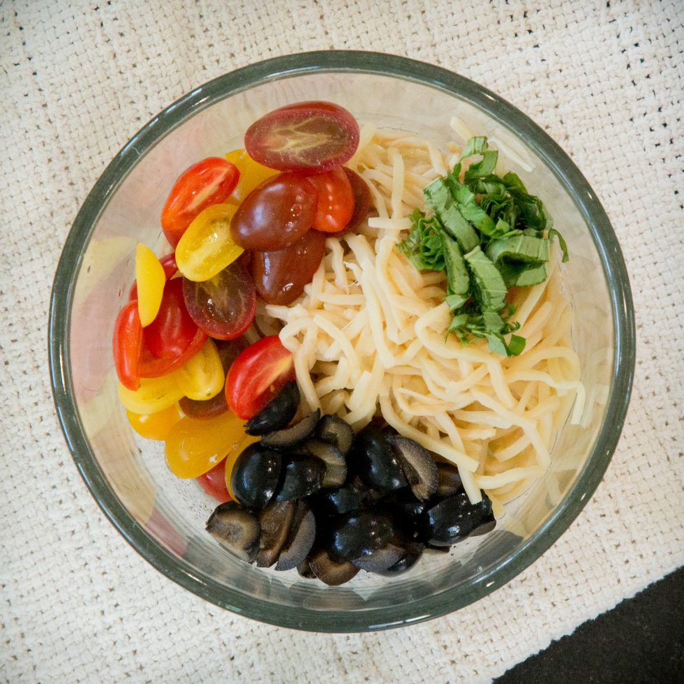 Adding the olives, tomatoes, and basil to the keto pasta salad.