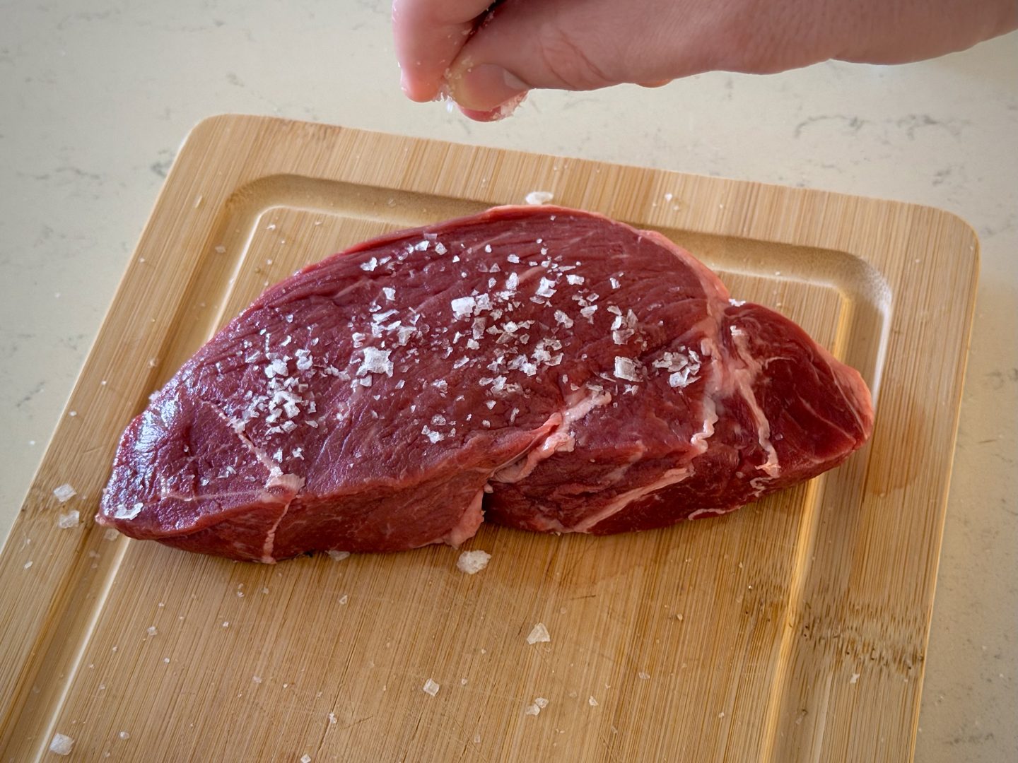hand sprinkling flaky salt onto raw steak